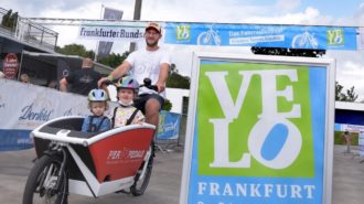 Foto: Velo Aufsteller und ein Mann mit Lastenfahrrad mit zwei Kindern vorne drin